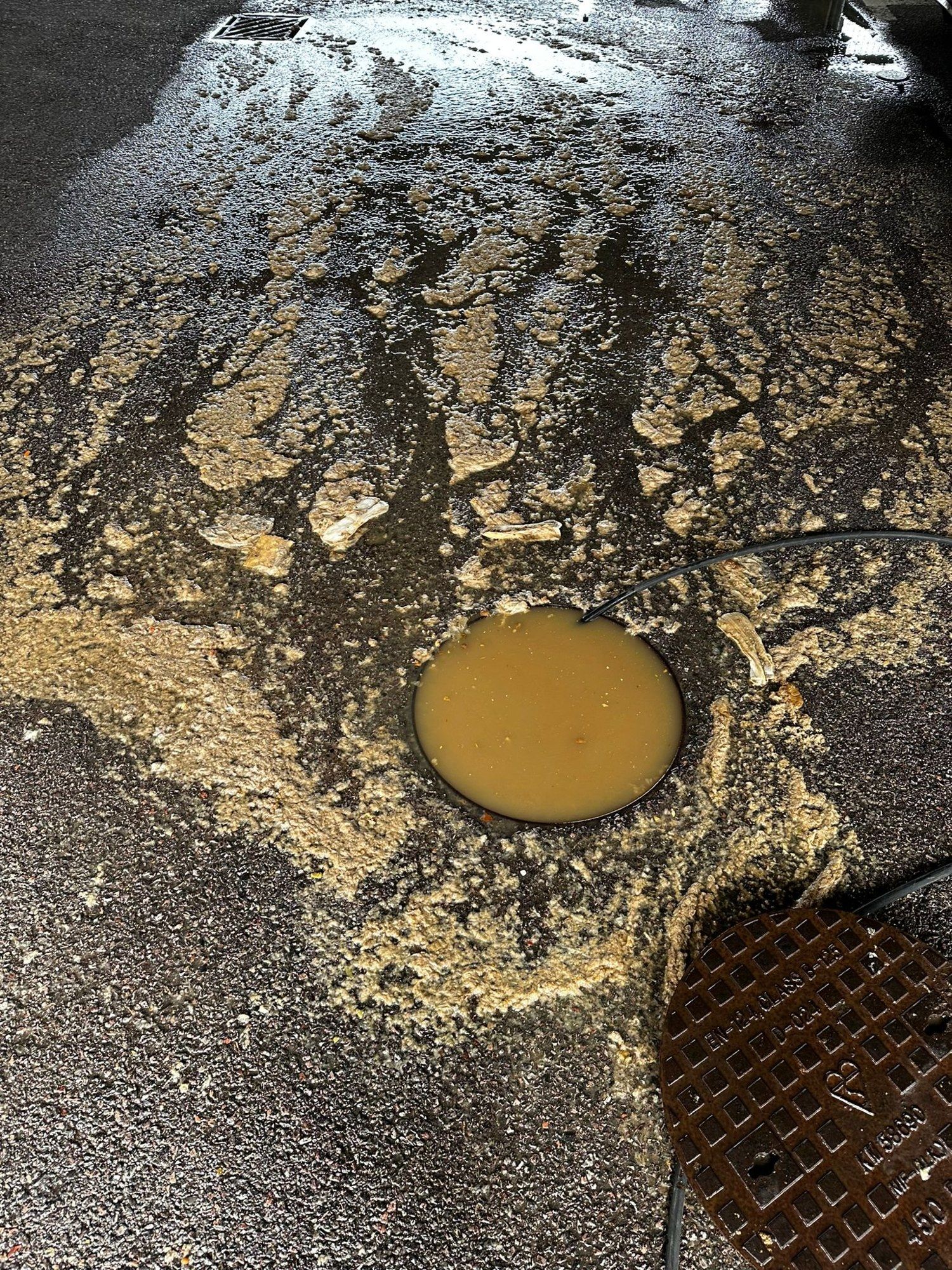 A blocked drain in a covered car park, with dirty water pooled over the grating