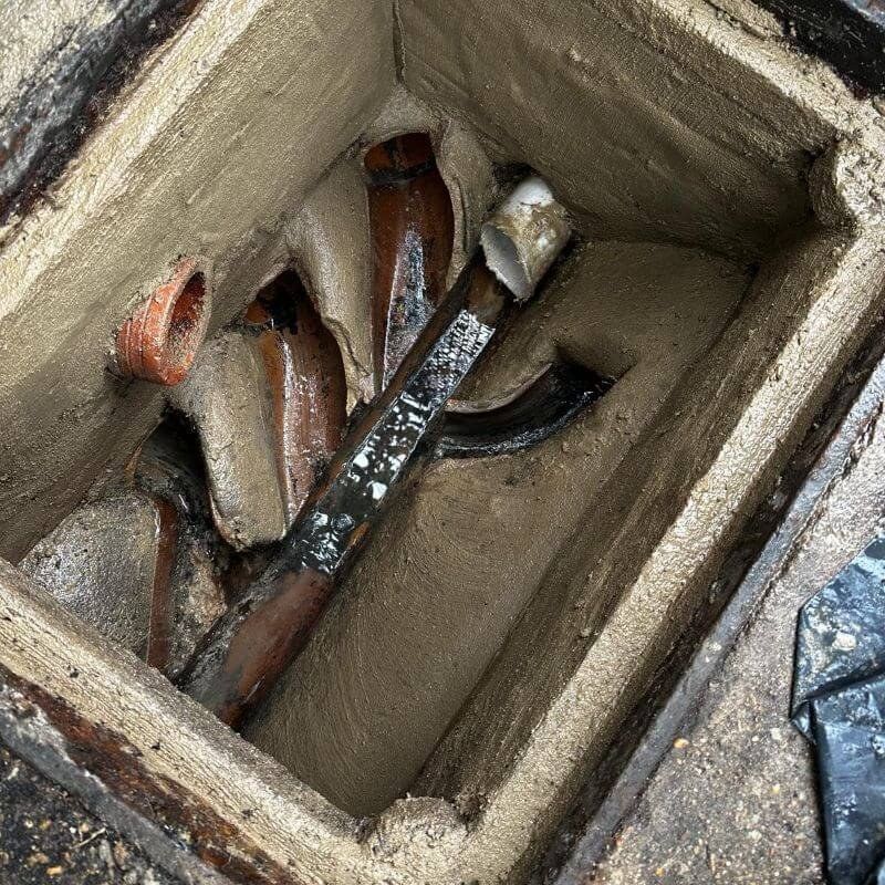 An open inspection chamber with clay pipes, cleared and the benching repaired