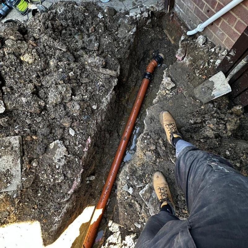 A trench dug beside a house exposing a gully and its pipework for repair