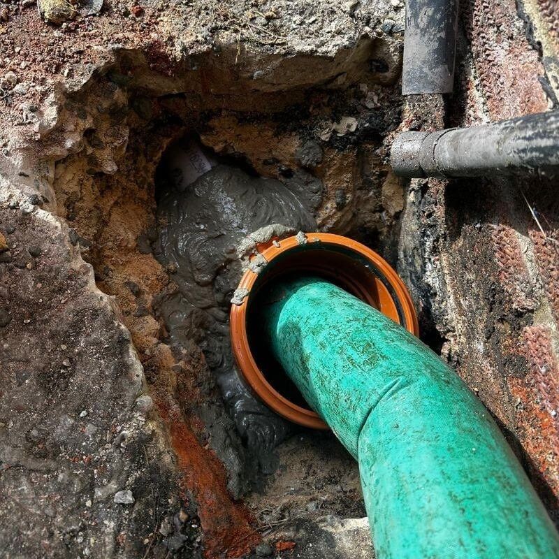 A green resin liner being fed into a drain pipe at an open excavation