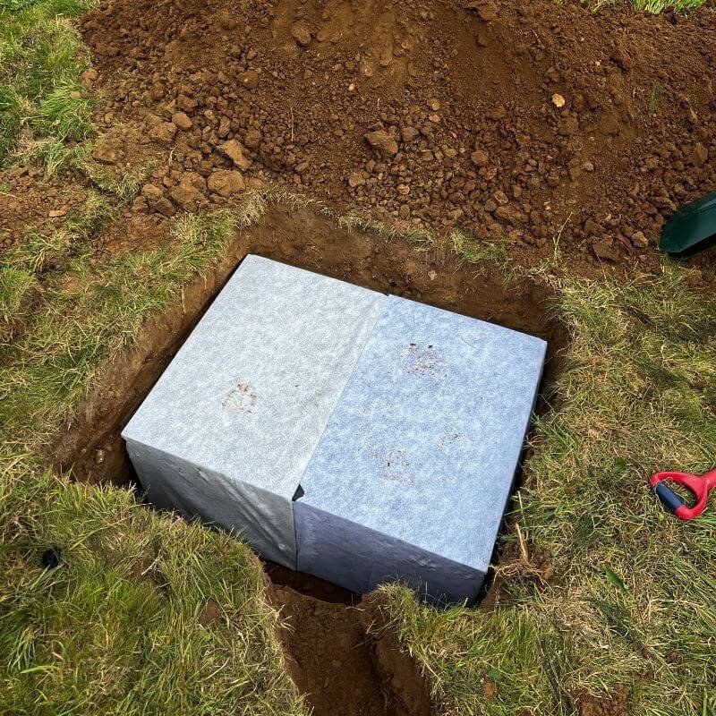 Soakaway crates wrapped in membrane, set in a freshly dug hole in a lawn